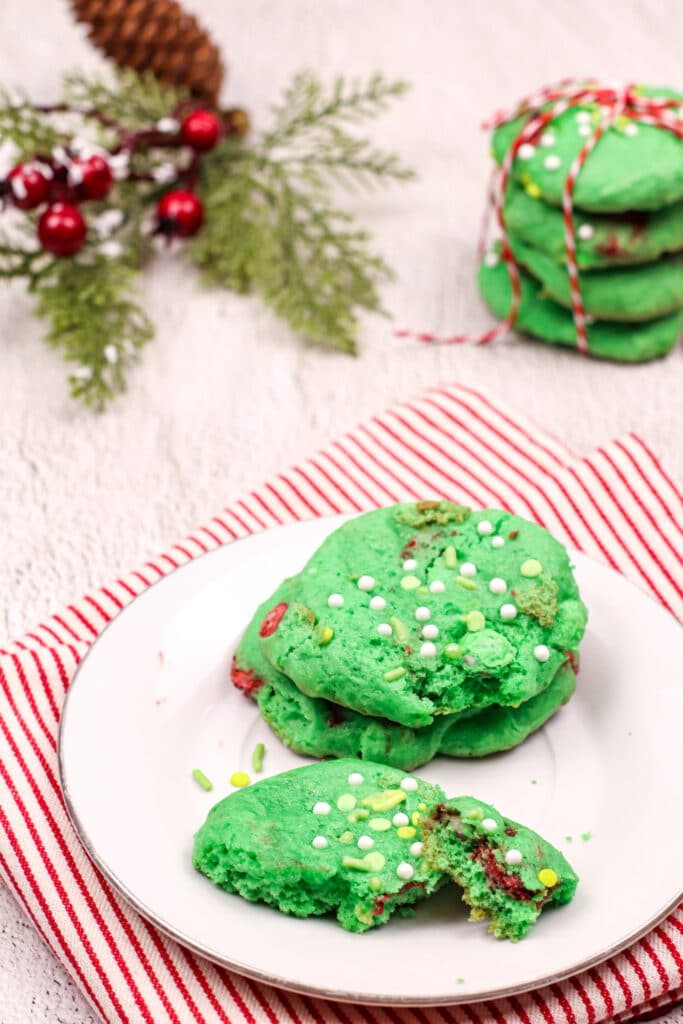 Three Grinch Cake Mix Cookies on a white plate with a red and white striped napkin