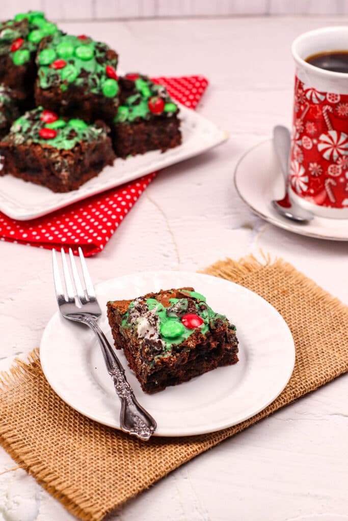 Grinch Brownie on a small white plate with a plate of brownies in the background