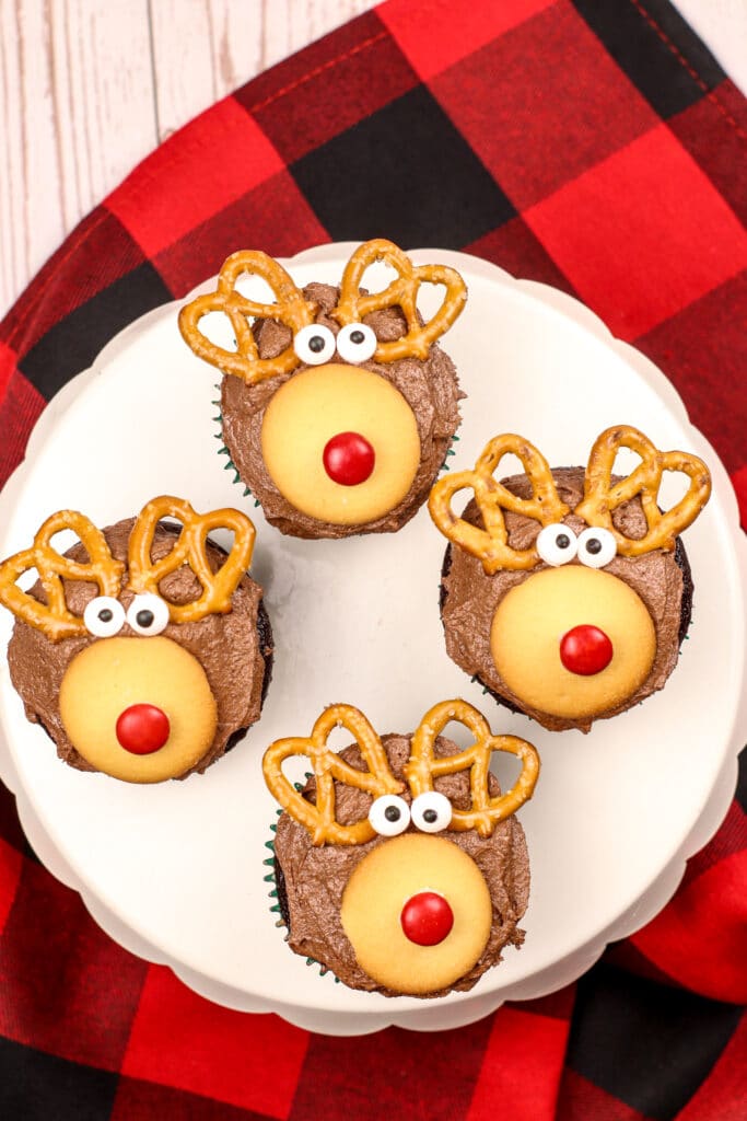 Four Rudolph Cupcakes on a white cake stand with a buffalo check napkin in the background