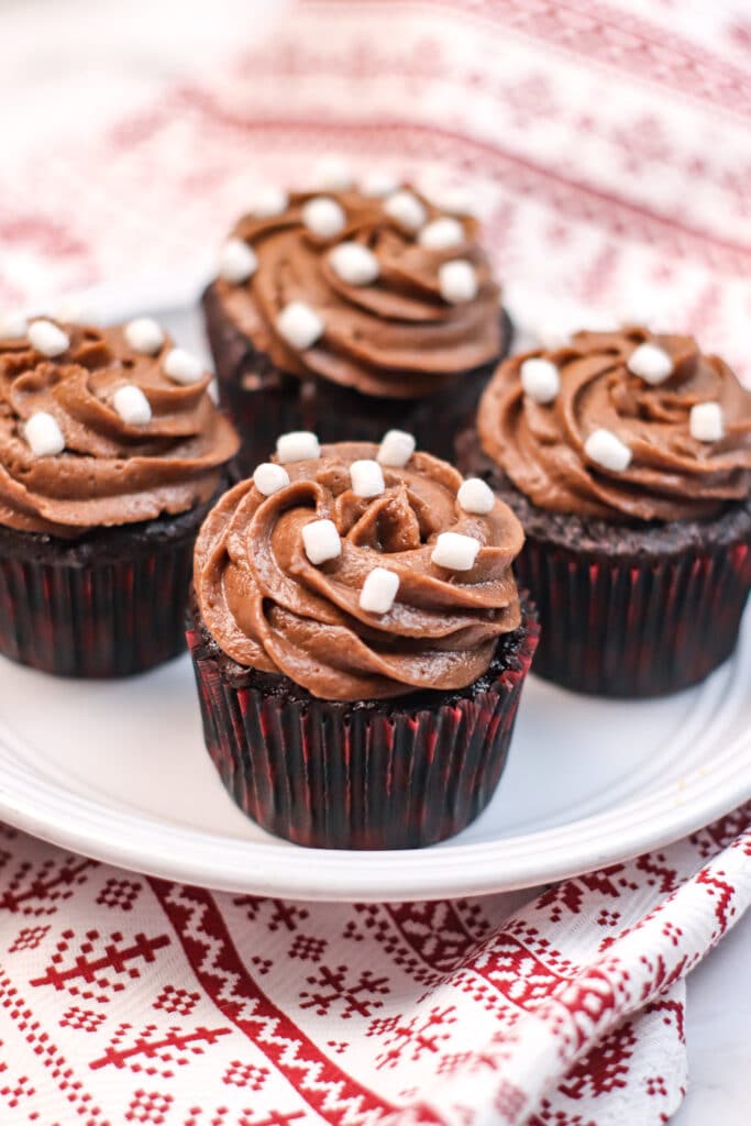 Four Hot Cocoa Cupcakes on a white plate on top of a Christmas Kitchen towel