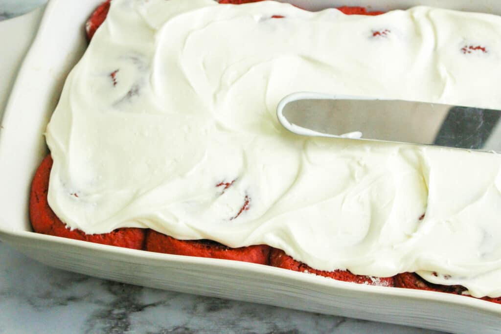 red velvet cinnamon rolls in white baking dish topped with cream cheese frosting
