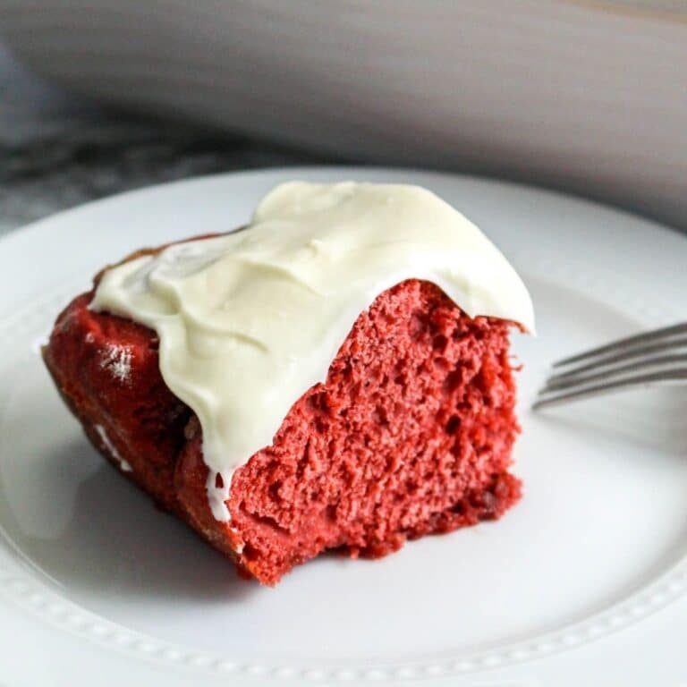 square image of a single red velvet cinnamon roll with cream cheese frosting on a white plate