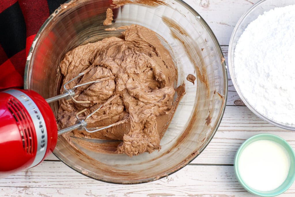 chocolate frosting in a glass mixing bowl with a red mixer