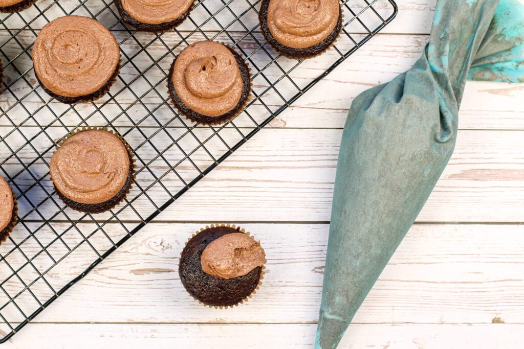 chocolate cupcakes on a cooling rack being frosted with chocolate frosting