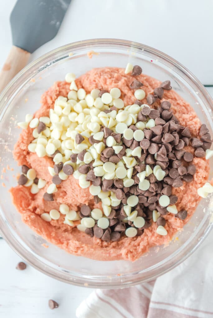 pink cookie dough in a glass mixing bowl with white chocolate and dark chocolate chips