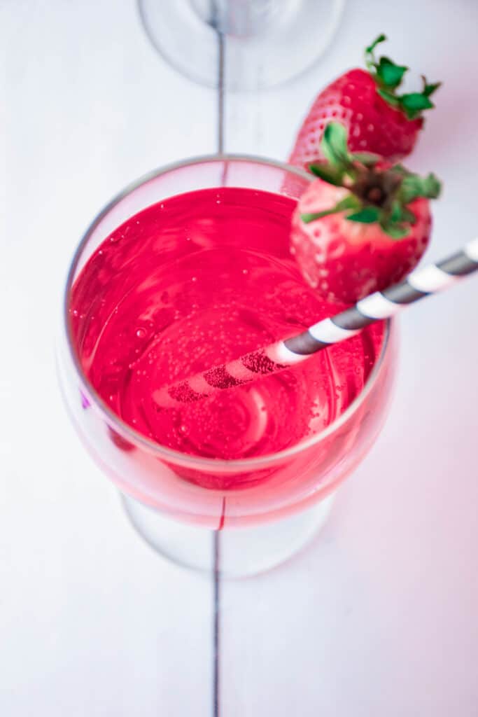 birds eye image of Cupid's Cocktail in a wine glass with a strawberry on the rim