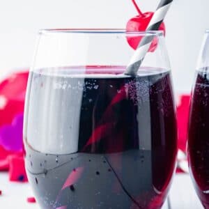 square image of glass of love potion with a black and white straw a cherry on the rim