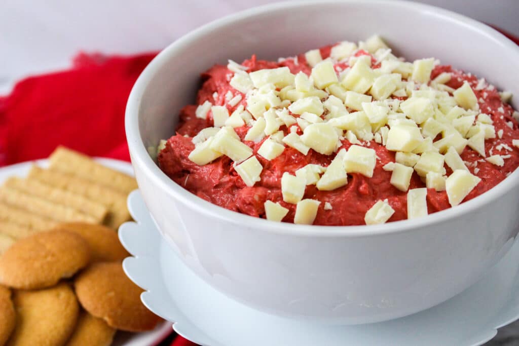 white bowl filled with red velvet cake batter dip, topped with chopped white chocolate