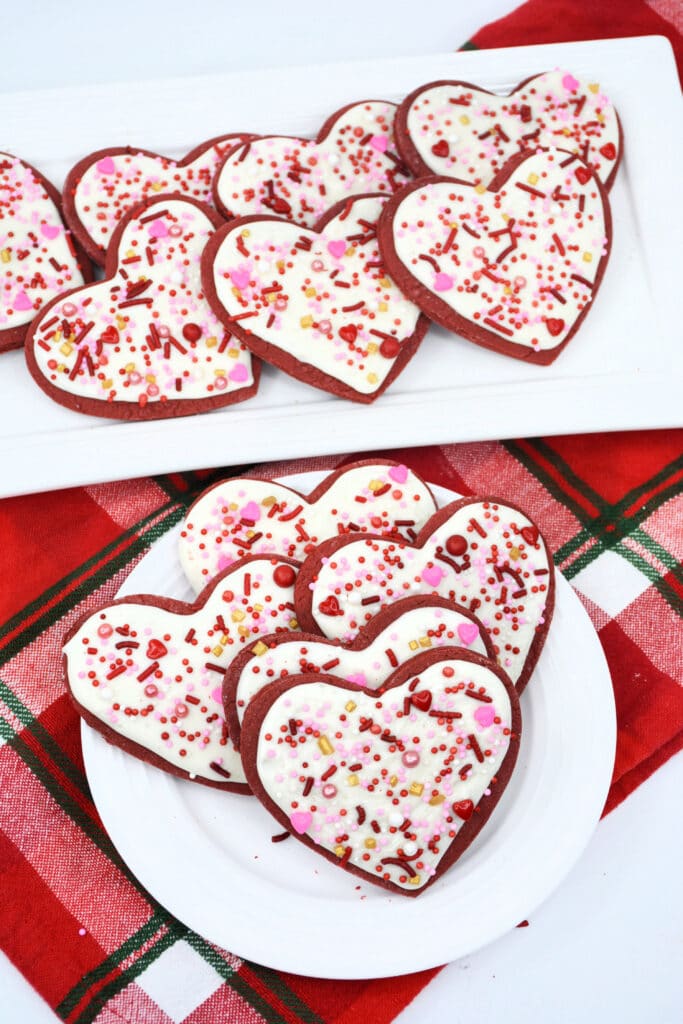 Heart-Shaped Red Velvet Cookies on a white plate with a rectangle platter of cookies in the background