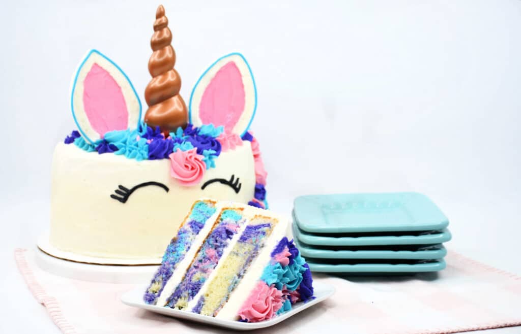 whole unicorn cake with a slice on a white plate in front of it.