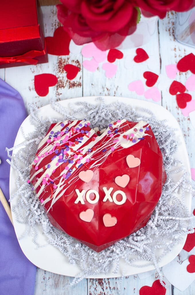vertical image of a red smashable heart with chocolate letters on the top