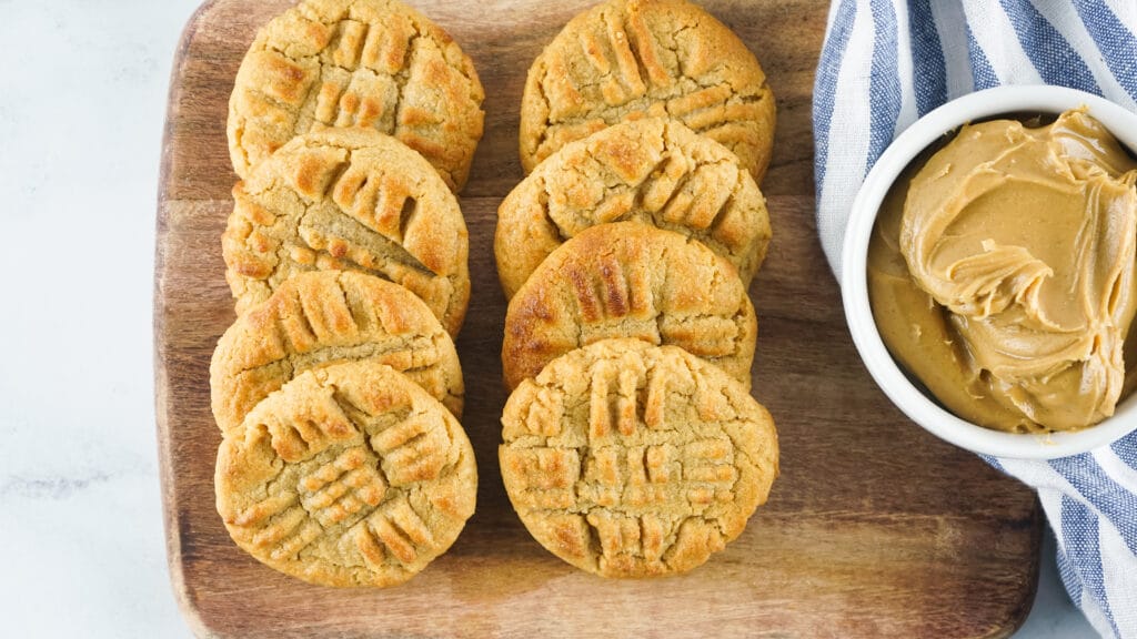 eight peanut butter cookies on a wooden cutting board with a small bowl of peanut butter next to them