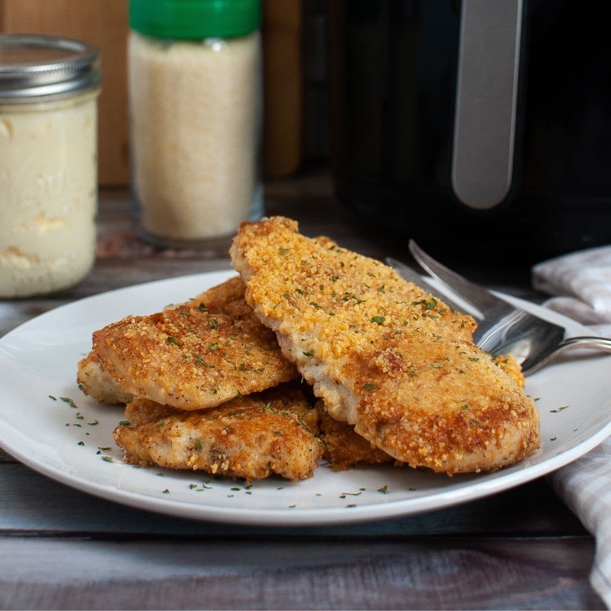 square close up image of three air fryer parmesan crusted chicken breasts on a white plate