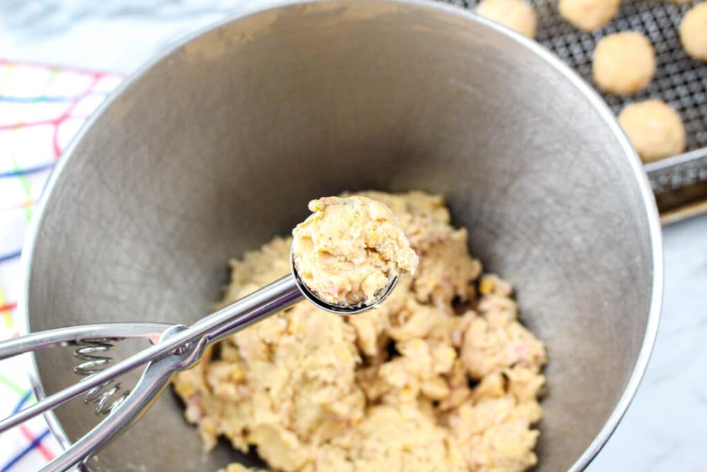 sausage ball mixture in a cookie scoop above a mixing bowl