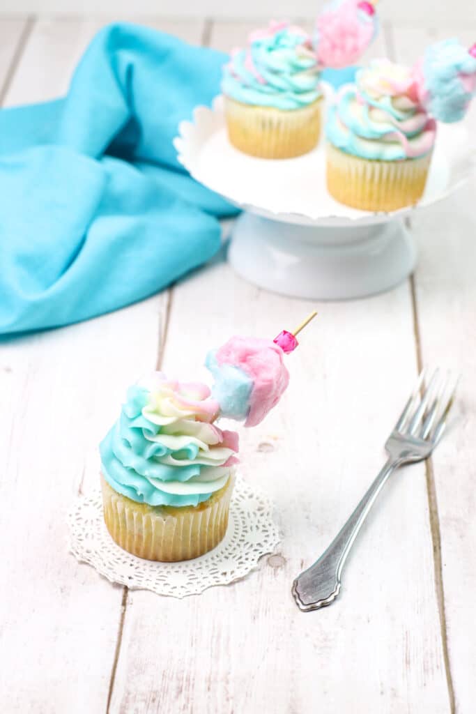 Vertical image of three cotton candy cupcakes on a wooden background