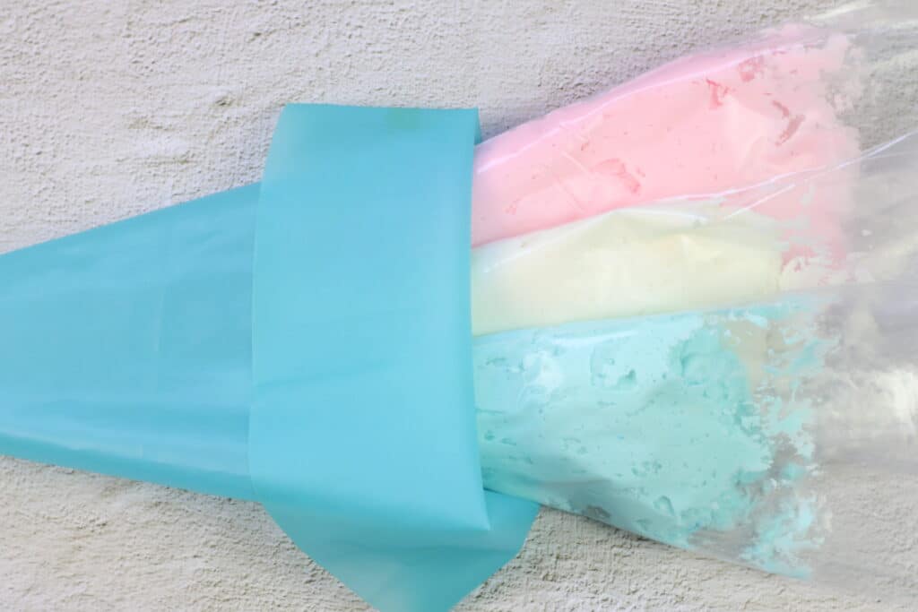 Pink, white and blue frosting in piping bags on a raised background