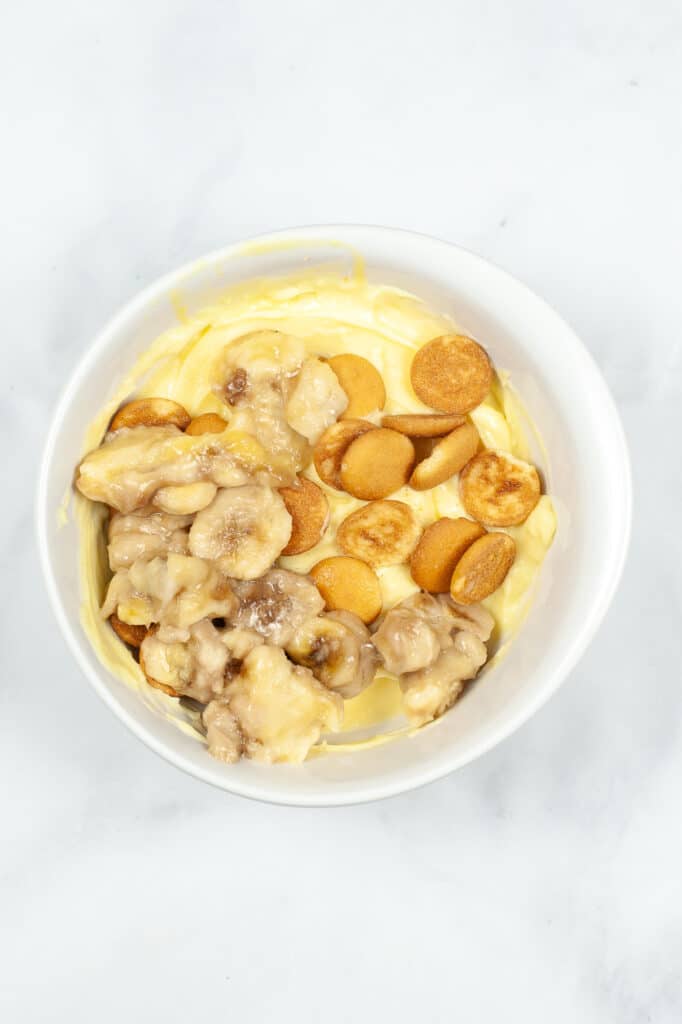 banana pudding, vanilla wafers and sliced bananas in a white mixing bowl