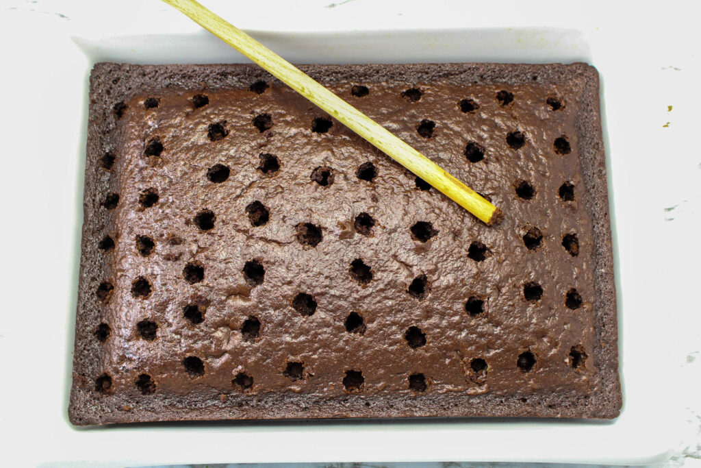 close up image of a wooden spoon laying on top of a chocolate cake with holes poked in it