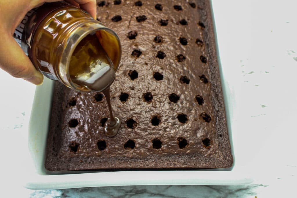 melted hot fudge being poured into the holes of a chocolate cake