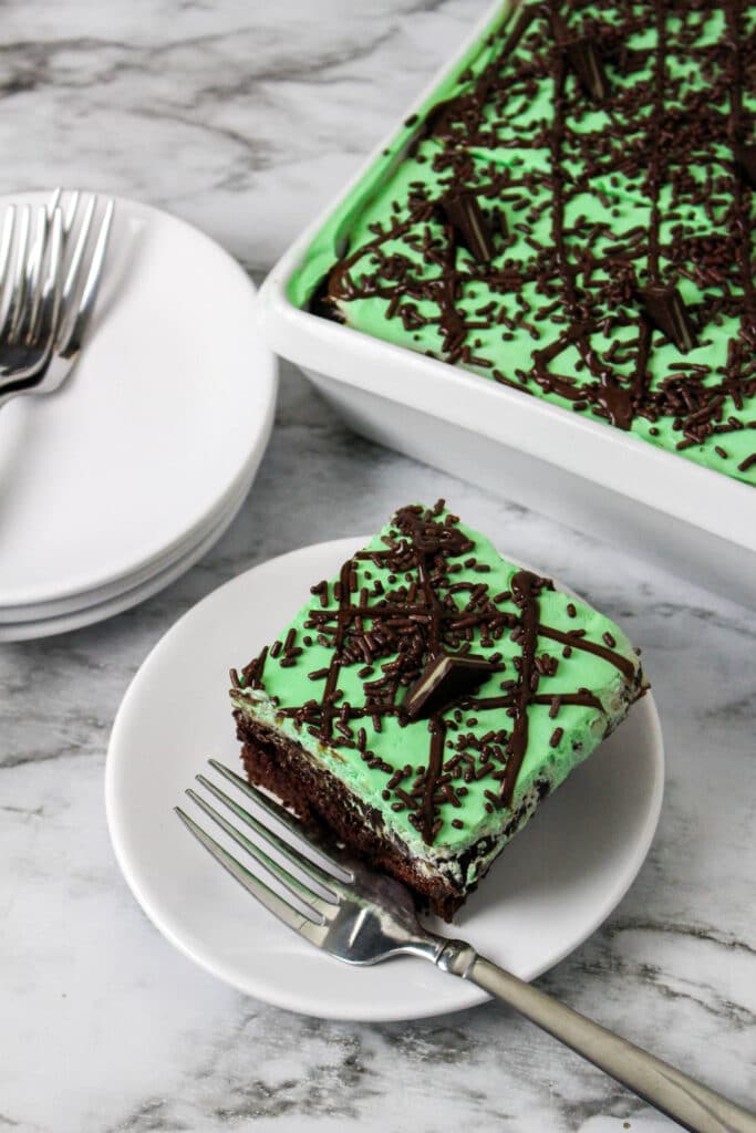 vertical image of a slice of grasshopper poke cake and the whole cake in the background
