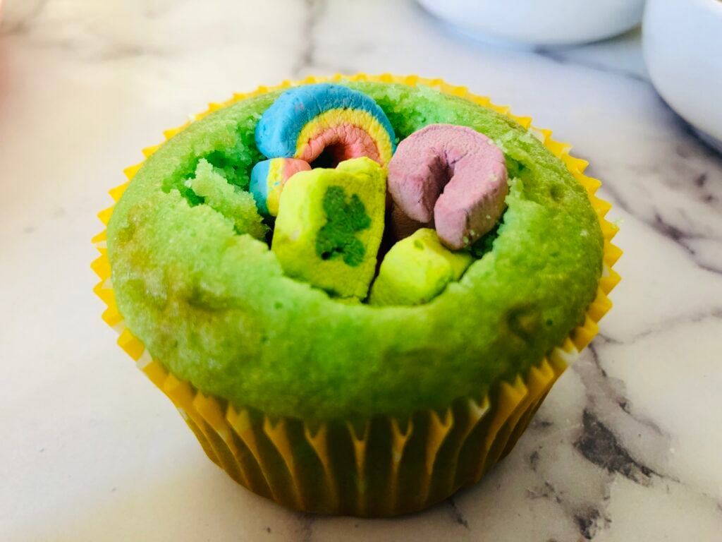 green cupcake being filled with lucky charms marshmallows