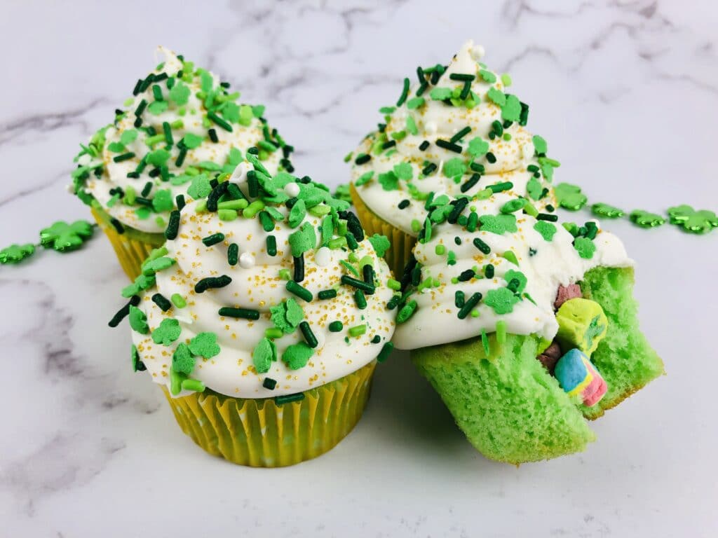 four lucky charms cupcakes with one broken up on a marble countertop
