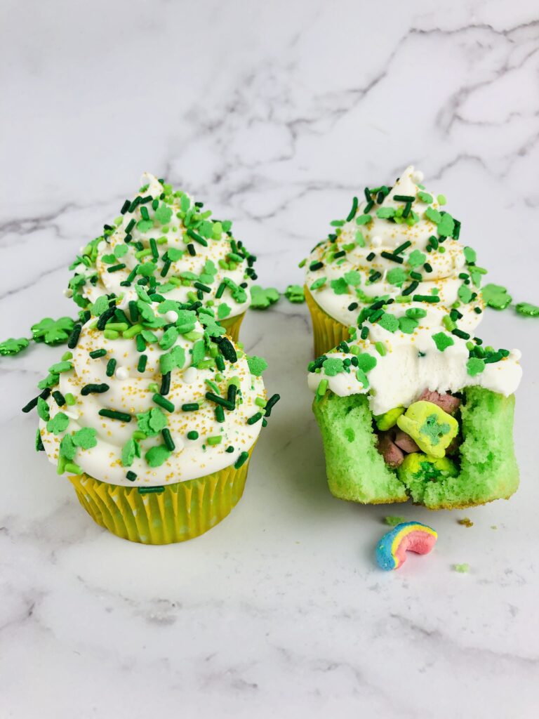 four lucky charms cupcakes on a marble countertop with one cupcake broken open