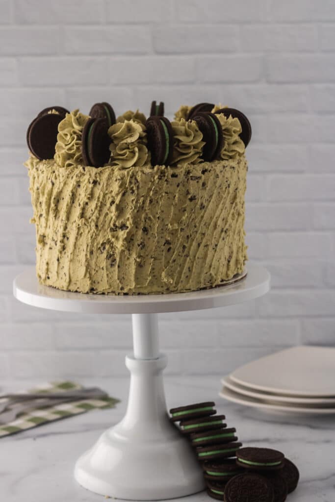 Mint Oreo Cake on a white cakes stand with mint oreos at the bottom