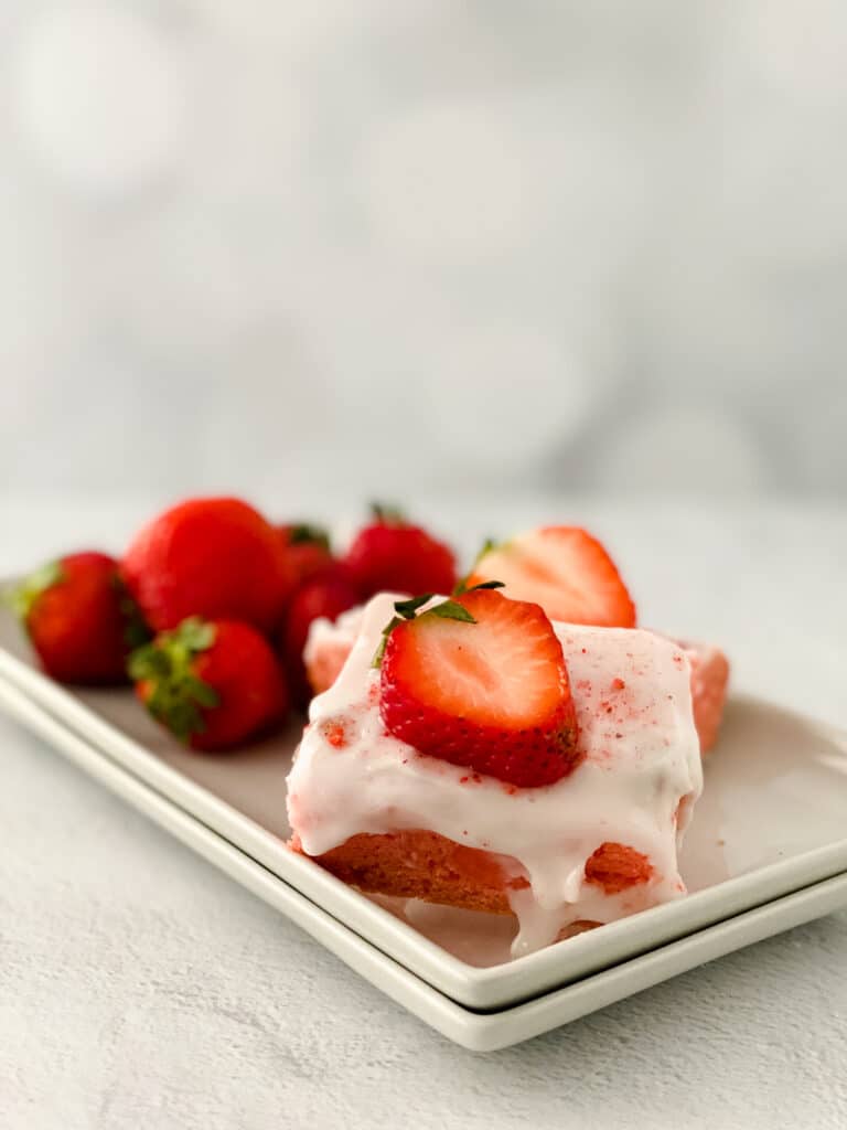 Two Strawberry Blondies topped with fresh strawberries on a white plate