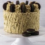 close up image of a whole Oreo Mint Cake on a cake stand with three mint Oreo Cookies