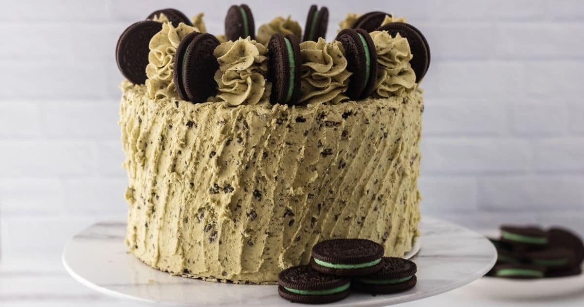 close up image of a whole Mint Oreo Cake on a cake stand with three mint Oreo Cookies