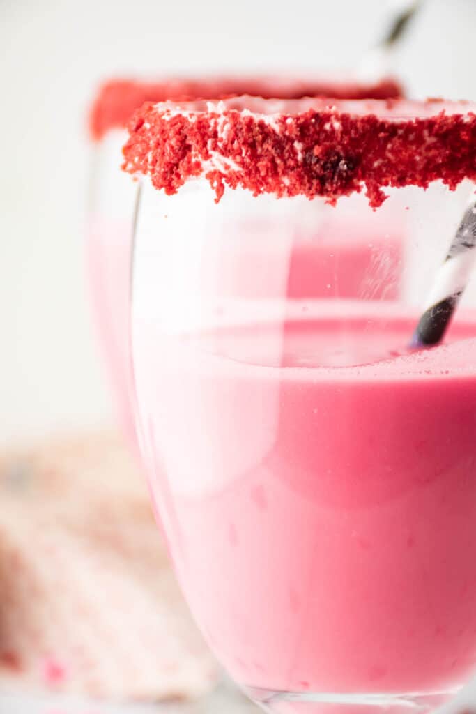 off center close up image of a glass of red velvet cocktail with a red velvet cake on the rim