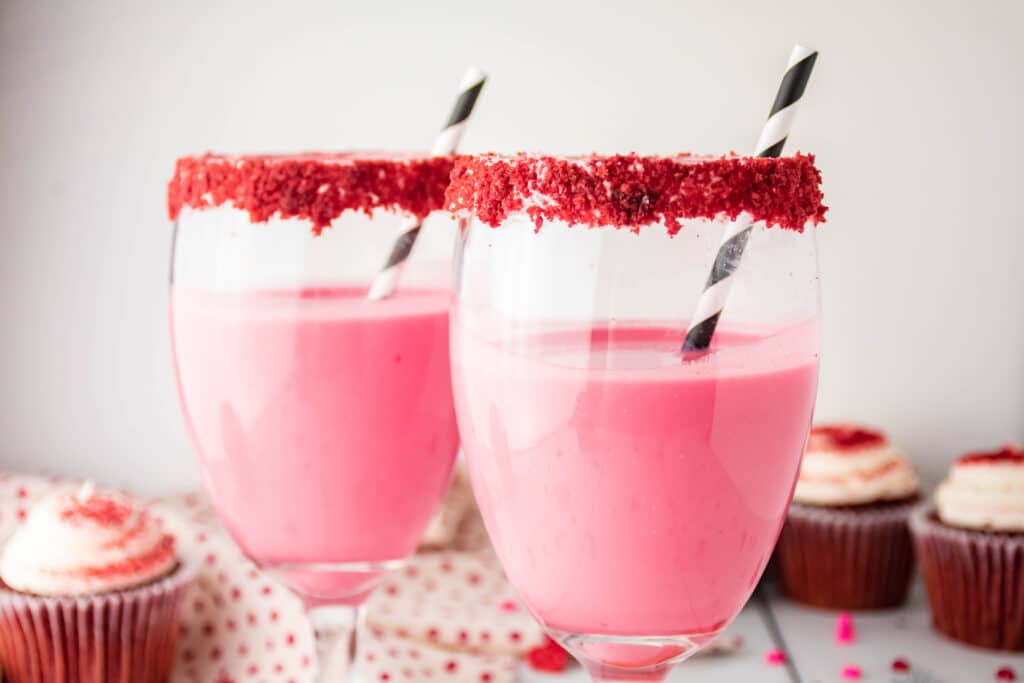 two glasses of red velvet cocktail with red velvet cupcakes in the background