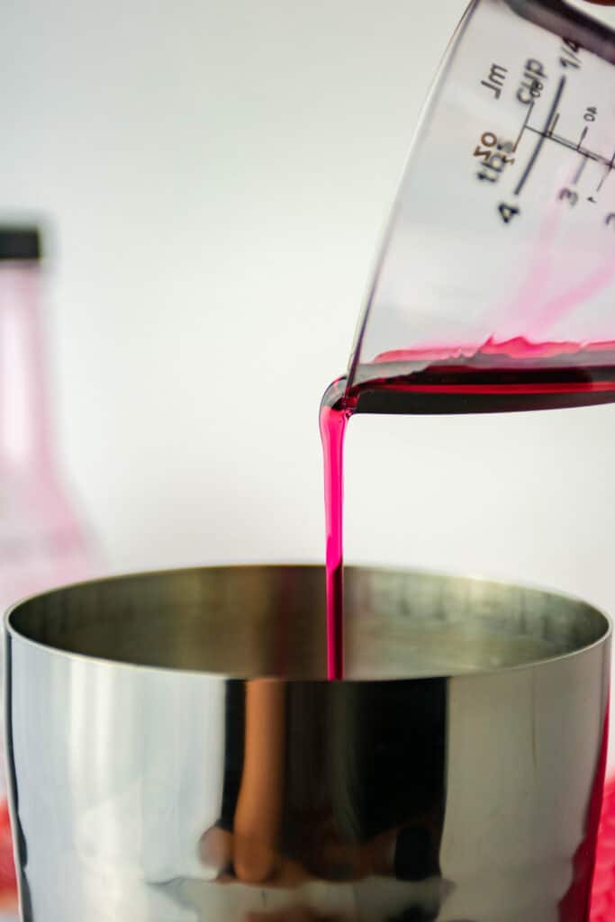 Grenadine being poured into a stainless steel shaker