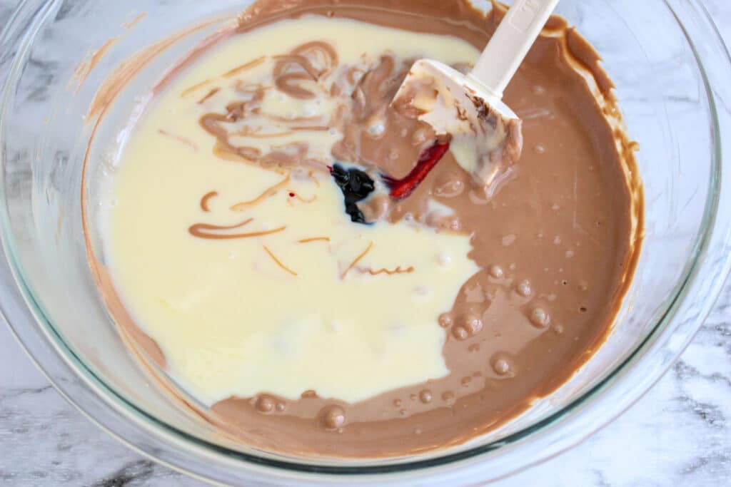 melted chocolate and white chocolate in a glass mixing bowl with red velvet paste