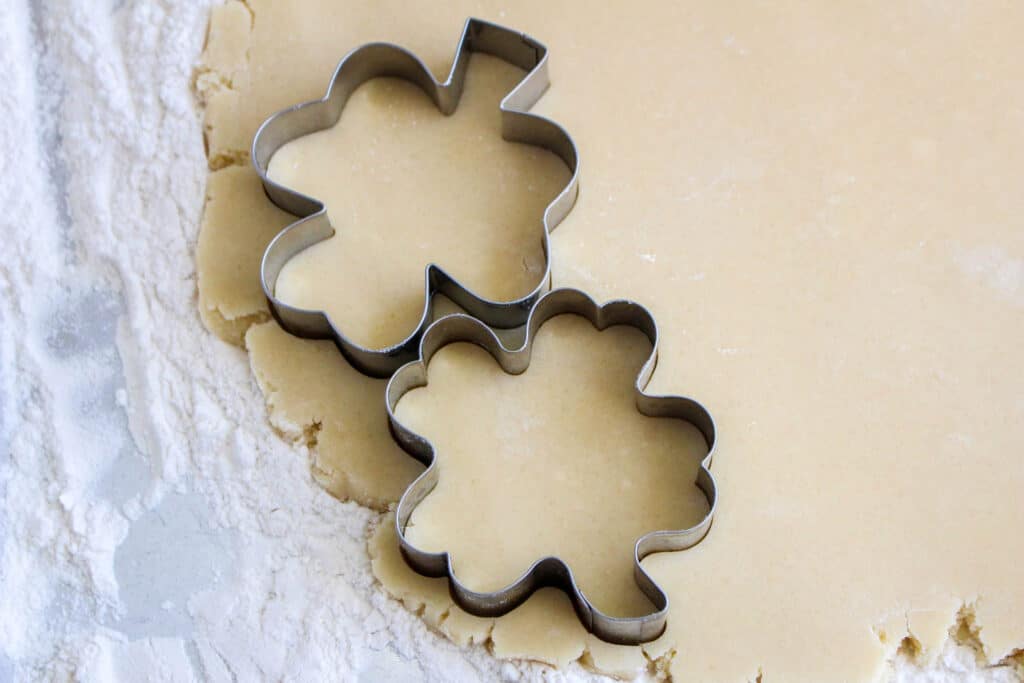 cookie dough rolled out and being cut with a shamrock cookie cutter