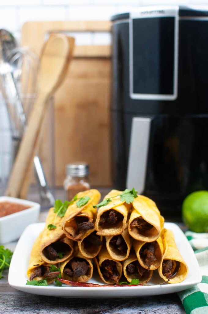 Air Fryer Beef Taquitos on a white plate with an air fryer in the background