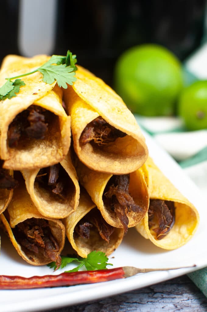 off center image of air fryer beef Taquitos stacked in a pyramid on a white plate