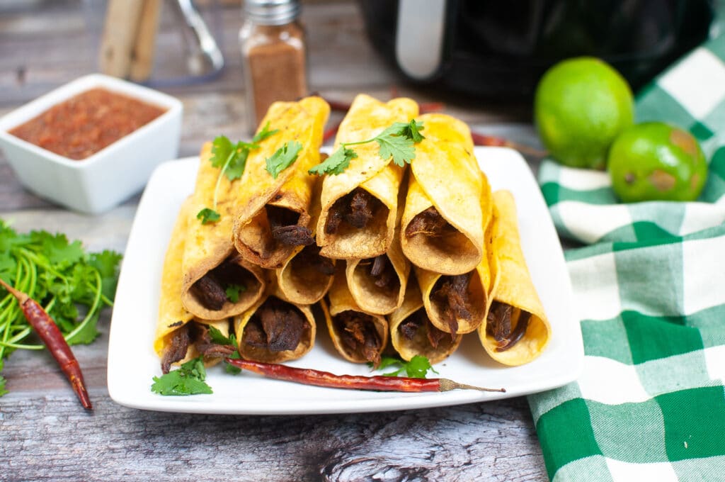 horizontal image of air fryer beef Taquitos stacked in a pyramid on a white plate