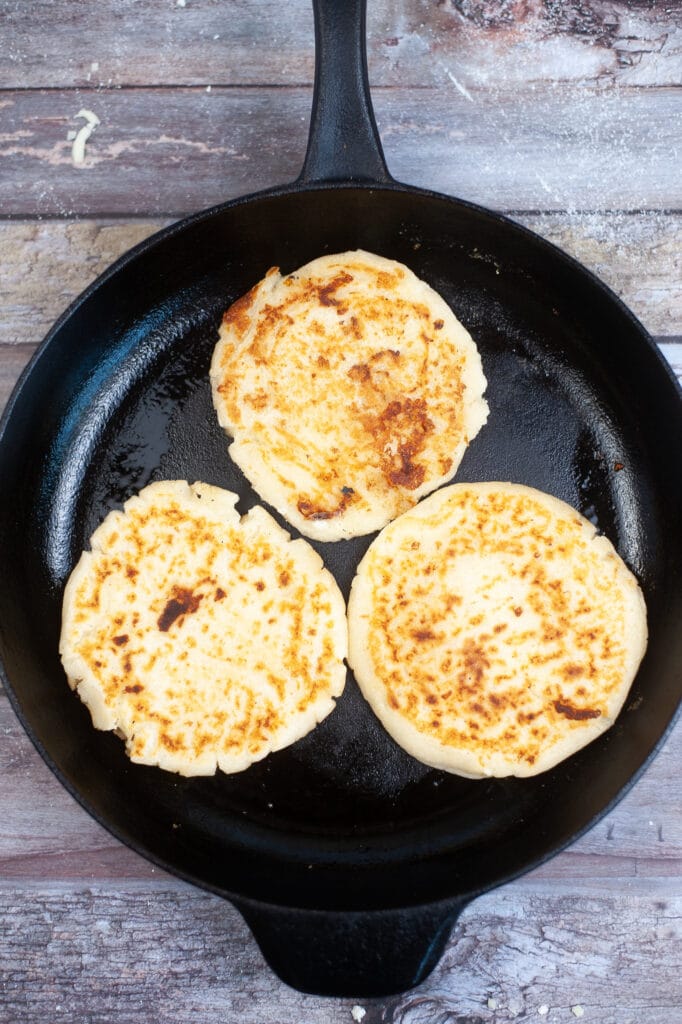 Arepas Con Queso being cooked in a cast iron skillet