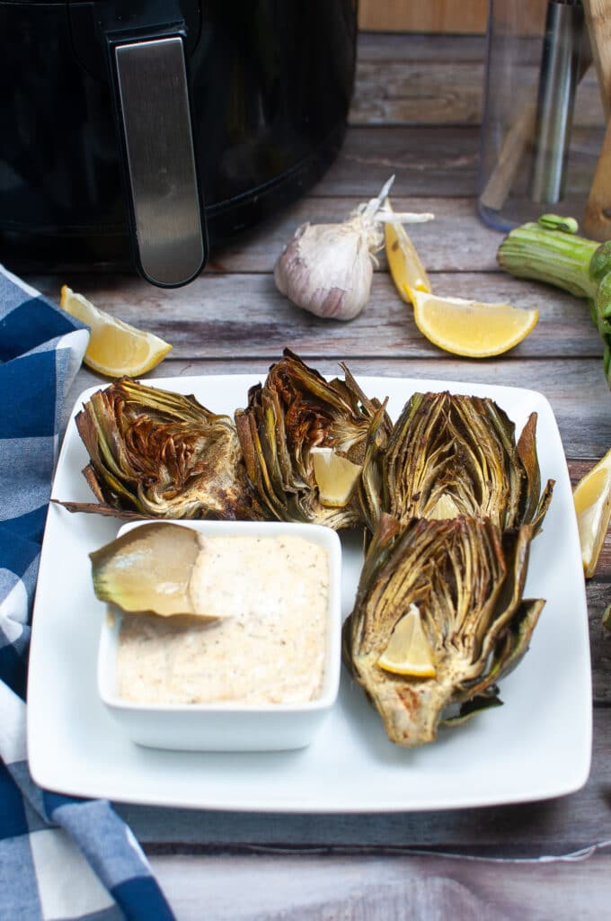 vertical image of two air fryer artichoke hearts on a white plate
