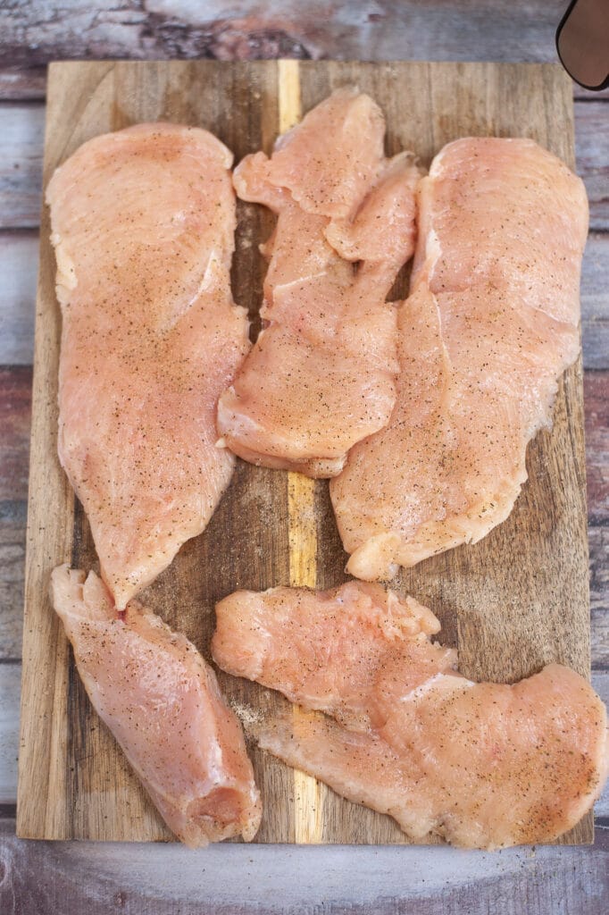 thin sliced chicken breasts seasoned with nature's seasoning on a wooden cutting board