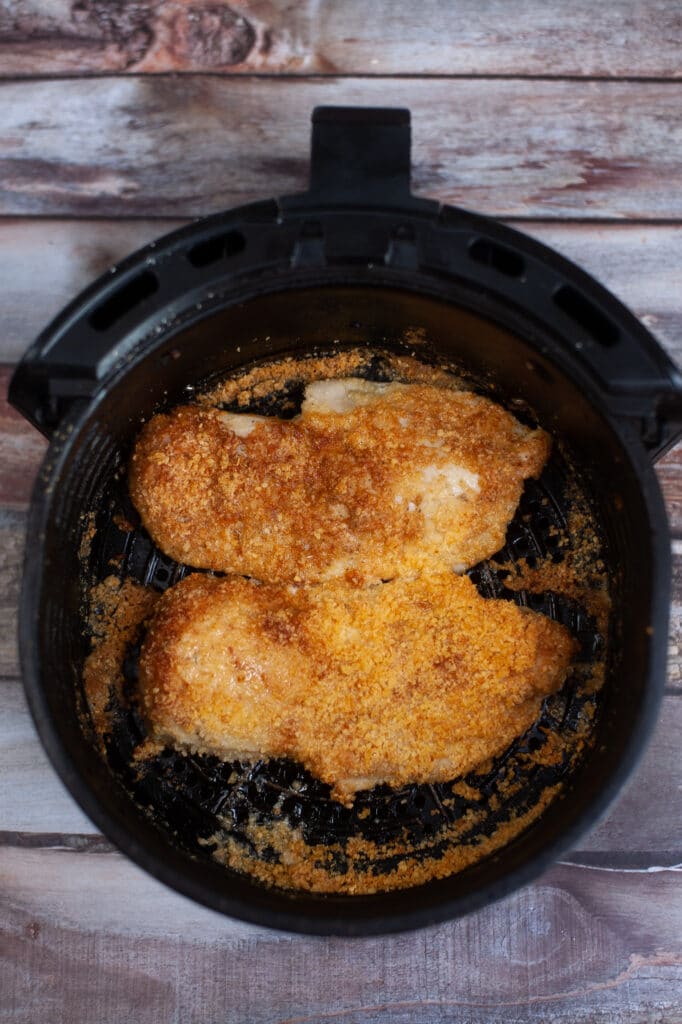 chicken breasts coated in parmesan cheese completely cooked in an air fryer basket