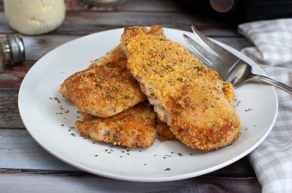 Three Air Fryer Parmesan Crusted Chicken Breasts on a white plate with parsley