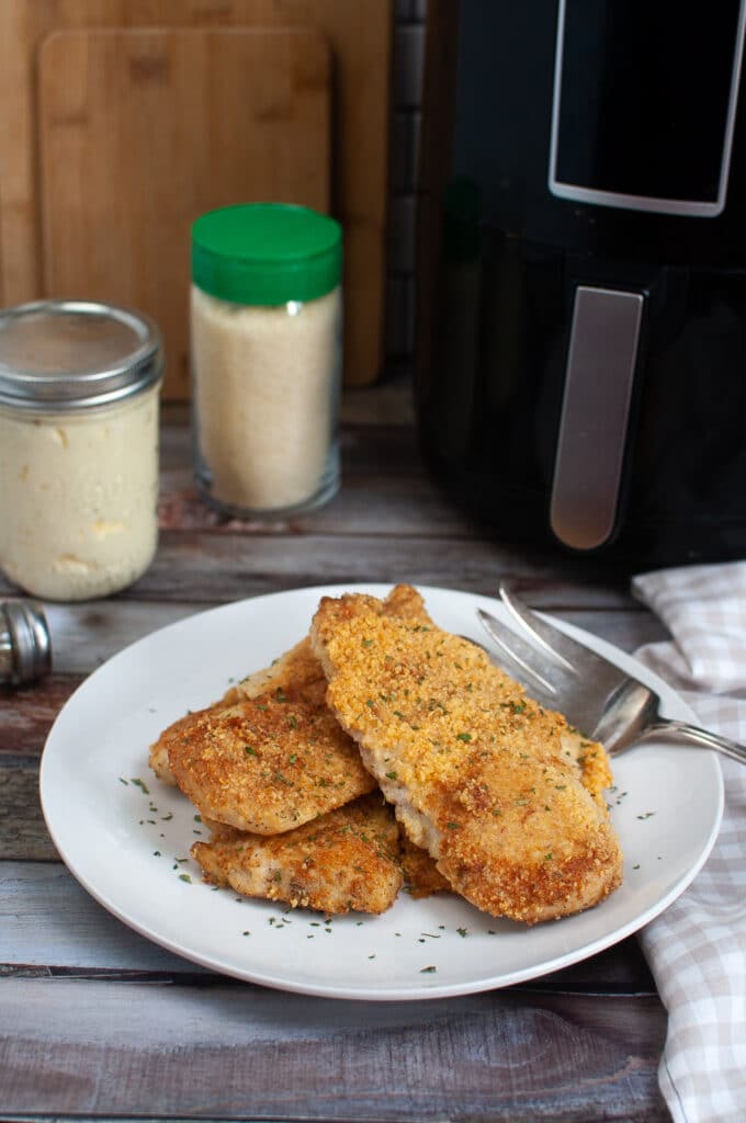 Air Fryer Parmesan Crusted Chicken Breasts on a white plate with an air fryer in the background