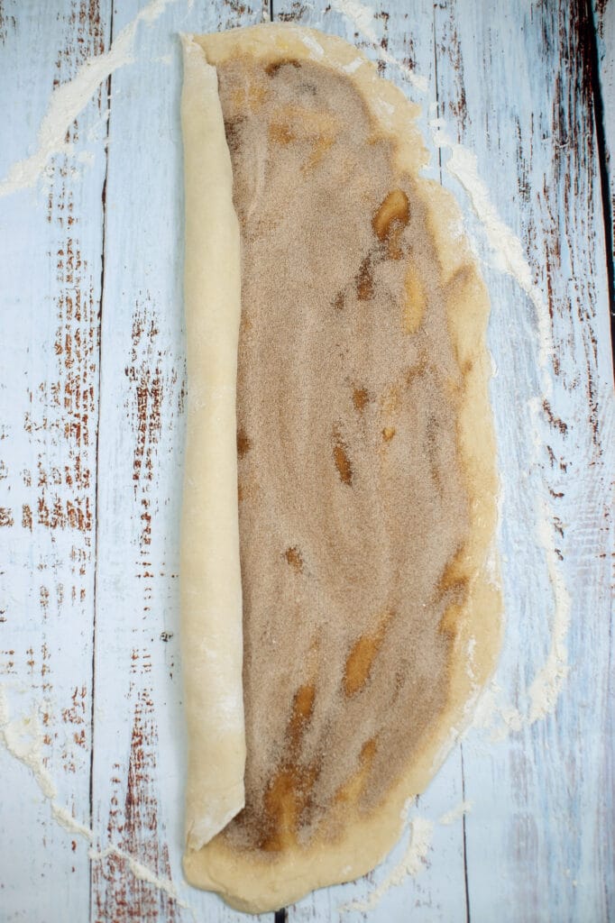 cinnamon roll dough being rolled up on a wooden background