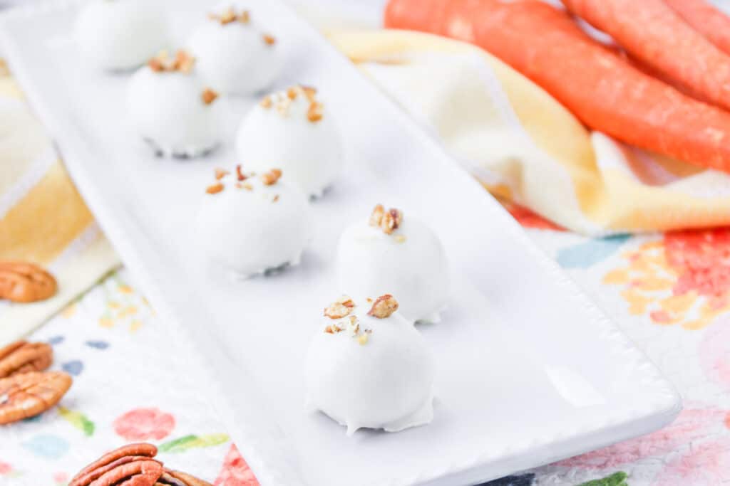 white carrot cake truffles on a white platter topped with nuts