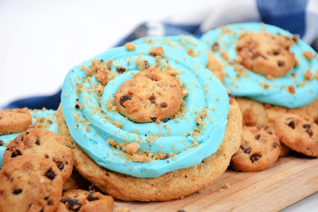 horizontal image of a Blue Monster Cookie on a wooden cutting board with mini chocolate chip cookies around it.