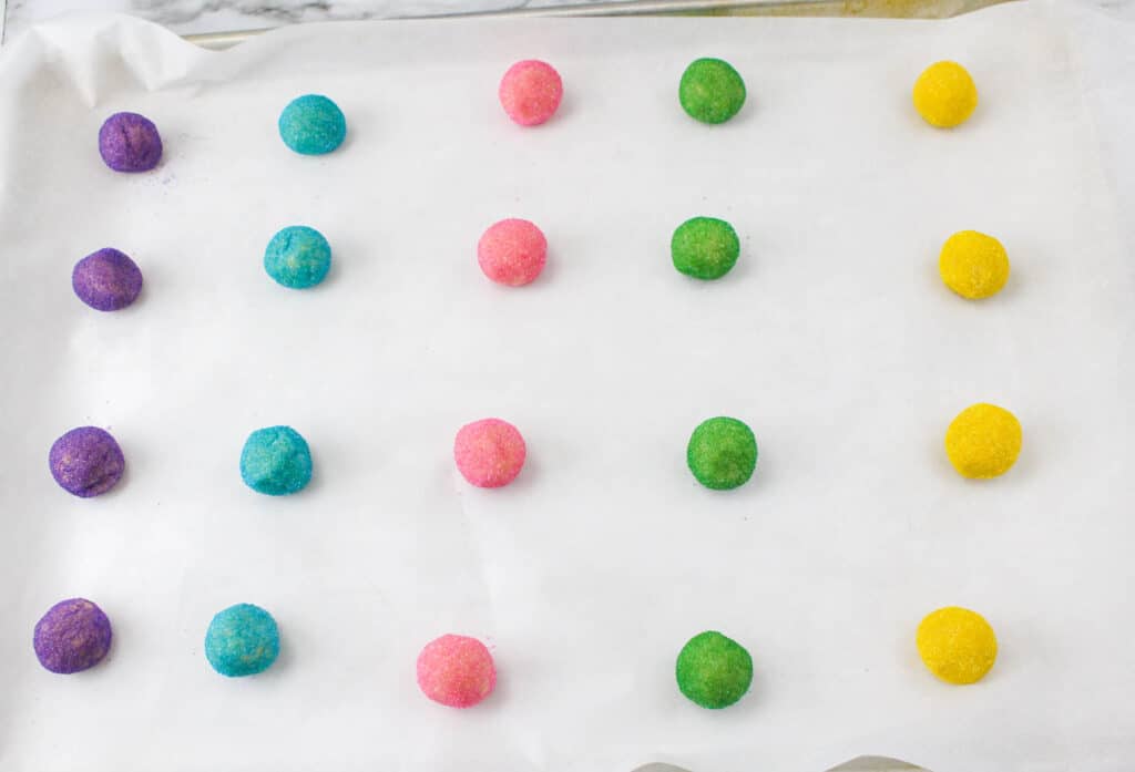 unbaked sugar cookie dough rolled in colored sugar on a parchment linted cookie sheet