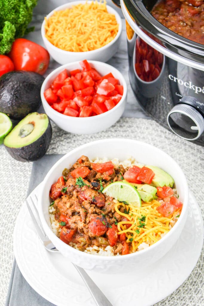 image of slow cooker carne picada in a white bowl with a crock pot in the background